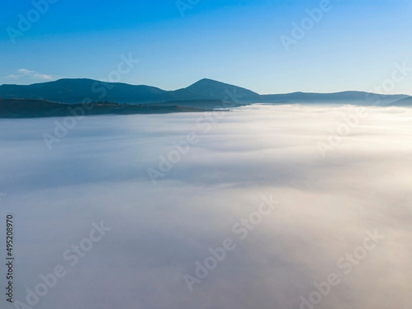 Fototapeta Flight over fog in Ukrainian Carpathians in summer. Mountains on the horizon. A thick layer of fog covers the mountains with a continuous carpet. Aerial drone view.