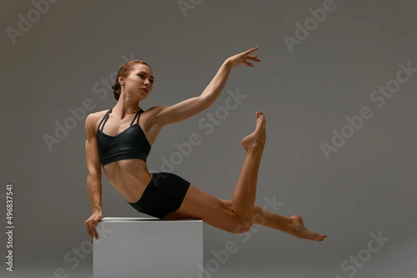 Fototapeta Beautiful athletic woman gymnast in sportswear performs gymnastics fitness exercises on a gray background. Sports motivation, stretching