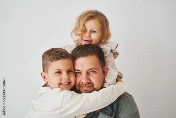 Fototapeta Close-up portrait of father, son and daughter. Happy family hugging and smiling on white background. Paternity. Single father bring up his children.