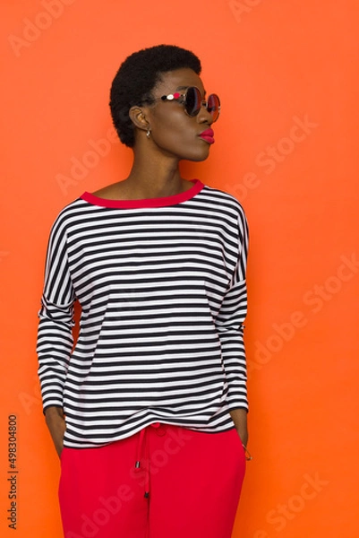 Fototapeta Young black woman in striped blouse and sunglasses is looking to the side.