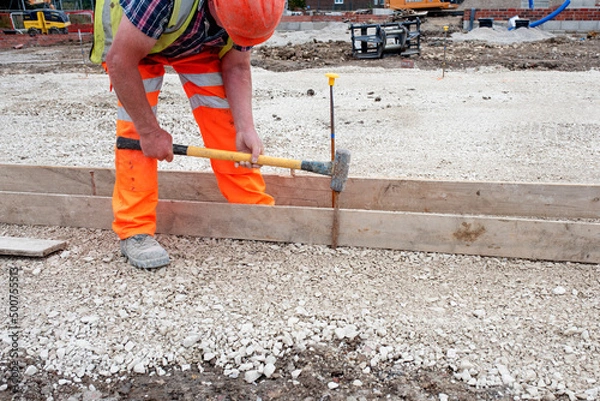 Fototapeta Groundworker making shutter for concrete to form a base for kerb using scaffold boards and steel road pins during new road construction