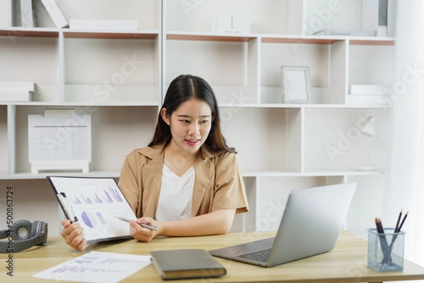 Fototapeta Online lifestyle concept A female home worker explaining her diagrams on the paper to her boss on the online meeting.