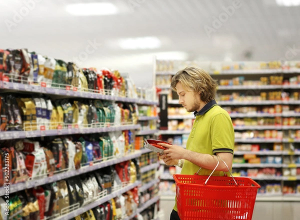 Fototapeta Young man shopping in supermarket, reading product information