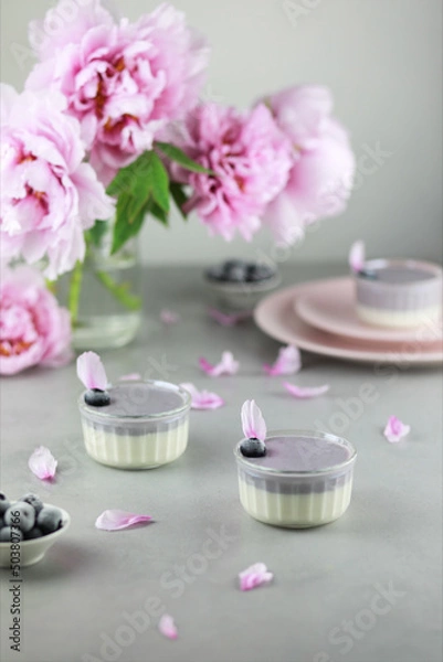 Fototapeta Homemade Italian dessert panna cotta with blue berries and bouquet of peony flowers on gray background. 