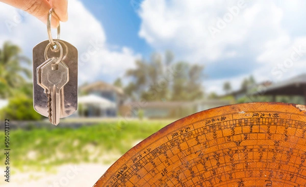 Fototapeta House key in girl hand with ancient feng shui compass over blurred house background, house feng shui