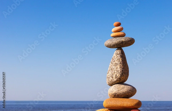 Fototapeta Rock zen Pyramid of balanced stones against the background of the sea and blue sky.