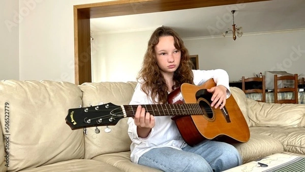 Fototapeta a fair-haired girl in a white shirt and jeans sits with a guitar she does not play it. High quality photo