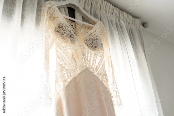 Fototapeta View of a bridal wedding dress hanging on the window. Wedding day concept.