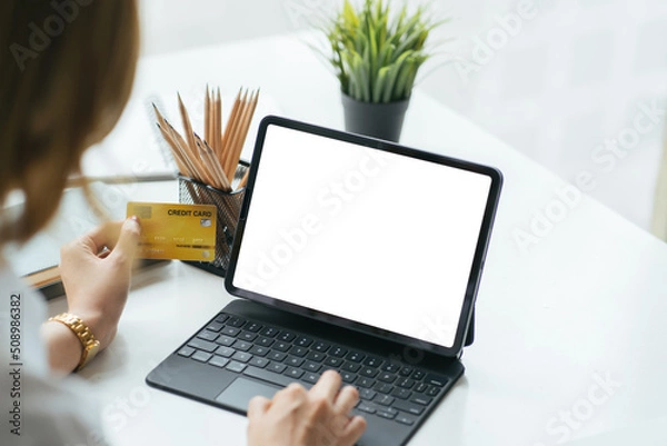 Fototapeta Mockup image of a woman holding credit card while using laptop with blank white screen in office.