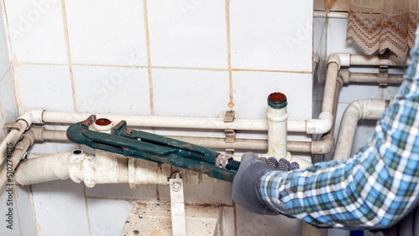 Fototapeta Worker uses an adjustable wrench to tighten the nut on the pipe of the water supply system in a private room