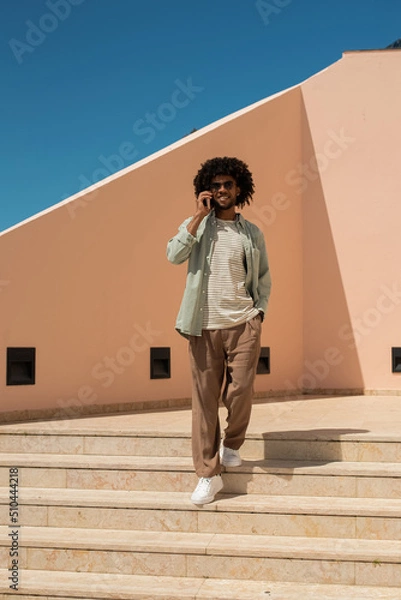 Fototapeta Happy African American man using cellphone outdoors. Man in casual clothes with beard holding mobile phone. Communication, technology concept