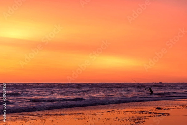 Fototapeta Fisherman silhouette from the shore with his rod at the seashore at sunset 