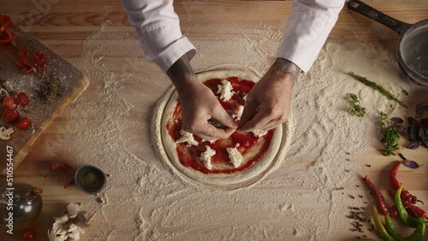 Fototapeta Professional chef prepare pizza dough on table. Man cook adding herbs in kitchen