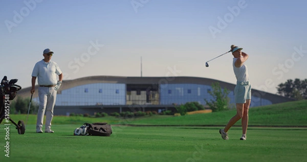 Fototapeta Golf team players hitting ball at golfing country club. Couple enjoy activity.