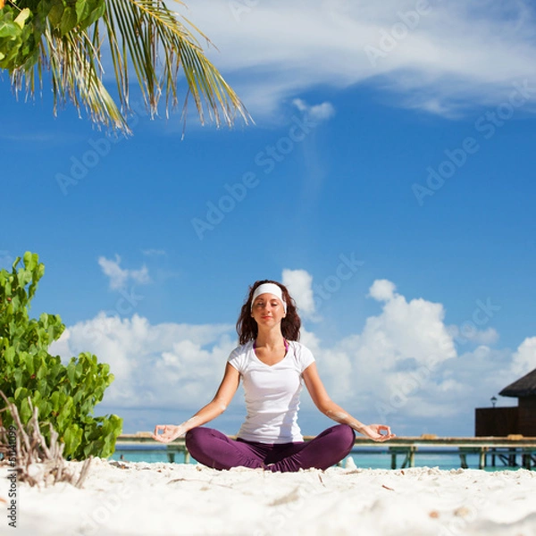 Fototapeta Pretty woman doing yoga exercises on the tropical  beach