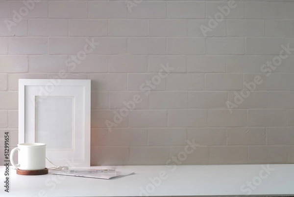 Fototapeta Minimal workplace with empty picture frame, coffee cup and notebook on white table.Copy space for your advertise text.