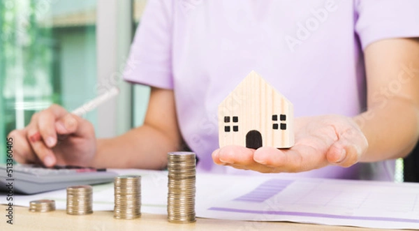 Fototapeta Miniature house beside stack of coins using as property real estate and financial concept. rent and purchase real estate concept. Home purchase mortgage concept. saving money and financial concept.