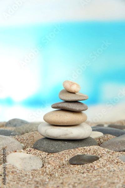 Fototapeta Tower of sea stones on sand on bright background