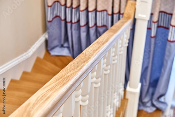 Fototapeta Wooden handrail of solid oak with white balusters. Classic style wooden staircase in a bright large room