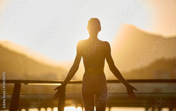 Fototapeta Meditation yoga woman silhouette on jetty during golden sunset with mountains view. Fitness and healthy lifestyle.