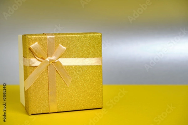 Fototapeta Golden gift box is tied with ribbon with bow silver background.