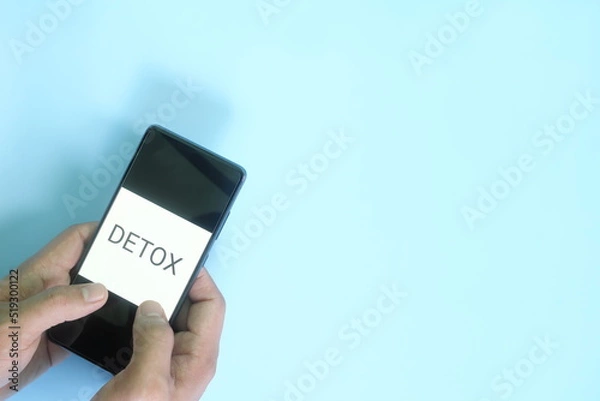 Fototapeta Digital detox concept. Hand holding a mobile phone in blue background flat lay.