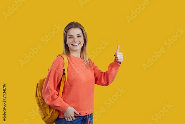 Fototapeta Happy content beautiful high school, college or university student girl with backpack standing on colour background, looking at camera, smiling and doing thumbs up. Education and success concept