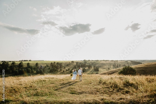 Fototapeta A young family with a little girl hugs and kisses on the field at sunset.