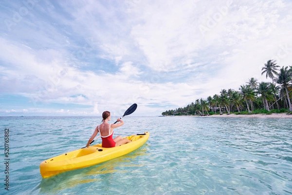 Fototapeta Young woman paddling the sea kayak in the tropical calm lagoon.