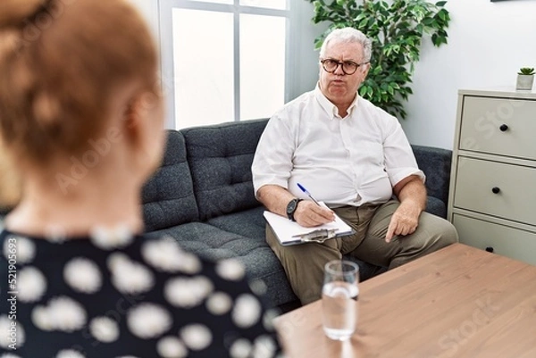 Fototapeta Senior psychologist man at consultation office puffing cheeks with funny face. mouth inflated with air, crazy expression.