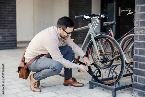 Fototapeta A casual businessman locks up his bicycle on the street.