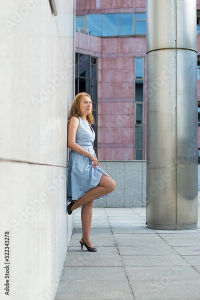 Fototapeta beautiful blonde posing in a blue dress on the street.