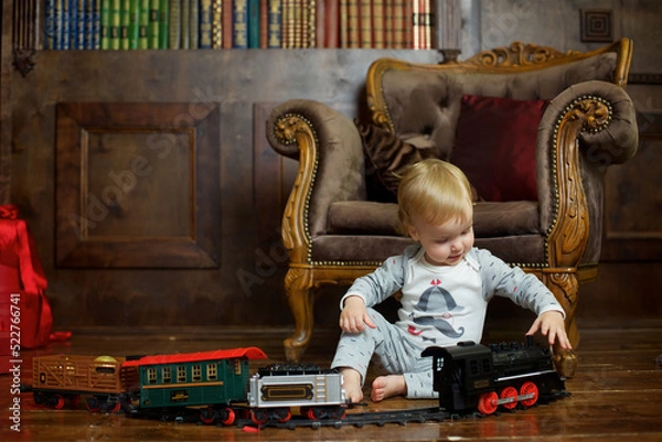 Fototapeta A small infant boy sits on the floor and plays a clockwork train.