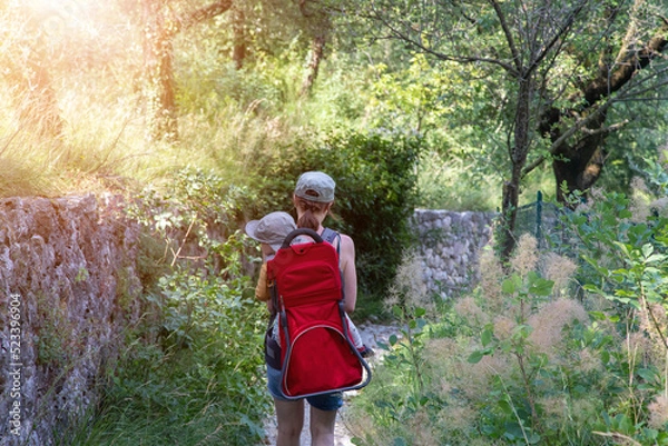 Fototapeta Family hiking in the Dolomites, Italy. Young mother is carrying her child in a hiking carrier on a trail