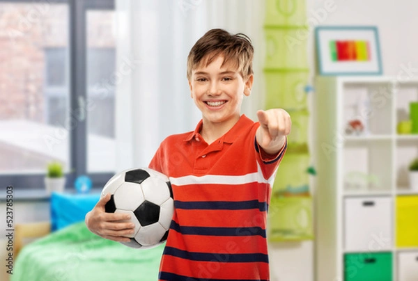 Fototapeta sport, football and leisure games concept - happy smiling boy holding soccer ball and pointing to camera over home room background