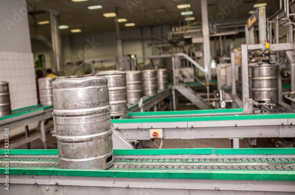 Fototapeta Brewery, bottling beer on aluminum kegs on conveyor lines. Industrial work, automated modern food and beverage production.