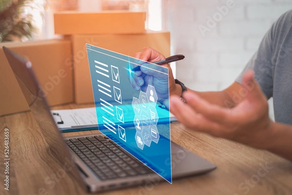 Fototapeta Smart checklist of business work on virtual screen,Close up hand a man holding pen mark on checklist in transport parcel delivery and use laptop working in office