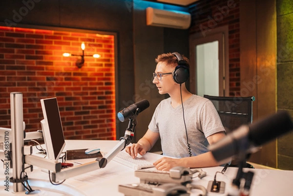 Fototapeta The DJ hosts the program and communicates with the audience on air at the radio station. The announcer reads the news. A male radio host speaks into a microphone and records a podcast