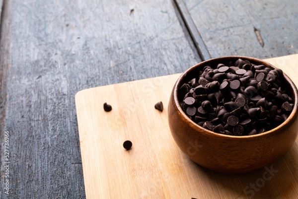 Fototapeta High angle view of chocolate chips in bowl on cutting board over wooden table