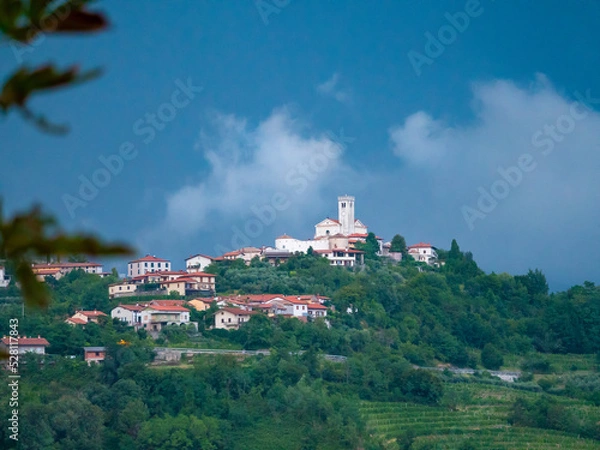 Fototapeta View of little town on hilltop surrounded with lush trees under dark blue sky