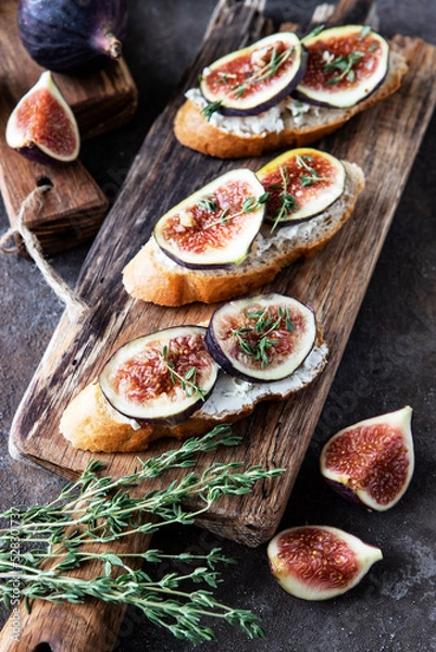 Fototapeta Breakfast with figs, cream cheese and honey toasts on a wooden board