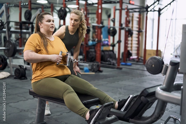 Fototapeta Caucasian plus size woman with her trainer working out in gym