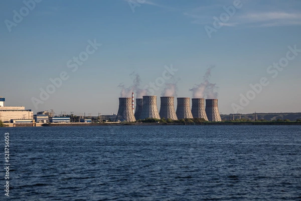 Fototapeta A beautiful nuclear power plant on the banks of the river. Big pipes. Power units of the station's atmospheric power plant. Sunny evening. Beautiful water.