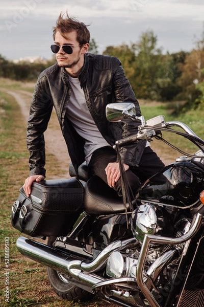 Fototapeta Handsome yong male is sitting on his motor bike outdoors