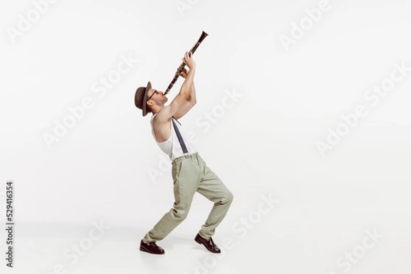 Fototapeta Portrait of young man playing clarinet isolated over white studio background. Stylish model