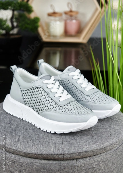 Fototapeta Stylish gray female shoes on gray pouf background in shop, copy space. New sneakers, close up. Beauty and fashion concept.