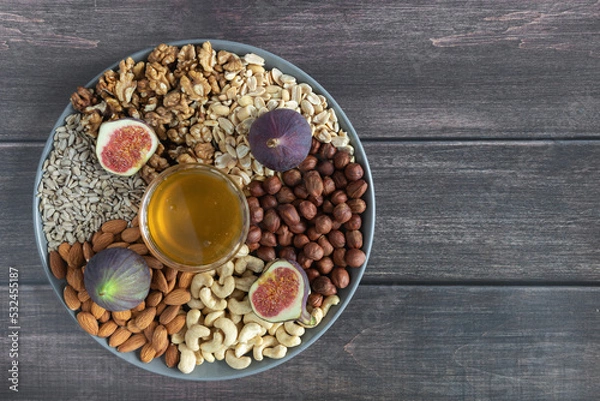 Fototapeta Flat plate with mixed nuts, honey, figs. Top view background with healthy snack on a wooden dark table