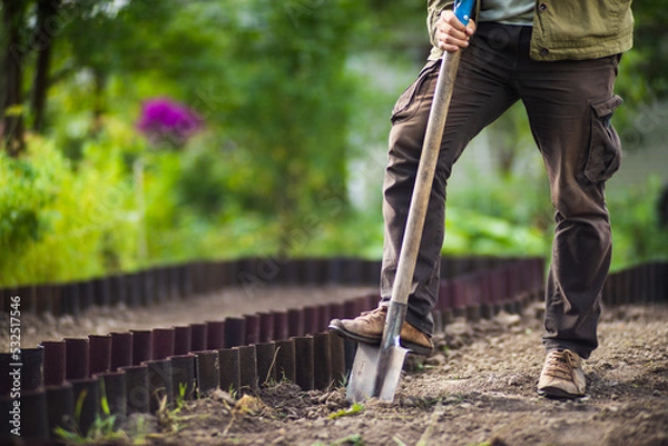 Fototapeta The farmer stands with a shovel in the garden. Preparing the soil for planting vegetables. Gardening concept. Agricultural work on the plantation