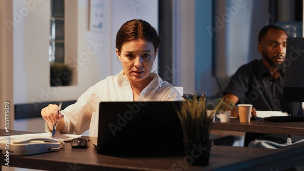 Fototapeta Woman attending online videocall meeting on laptop, talking to people on webcam with remote videoconference call at night. Chatting on teleconference chat, internet telecommunications.