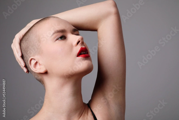 Fototapeta Headshot of beautiful young bald woman looking aside and posing indoor.